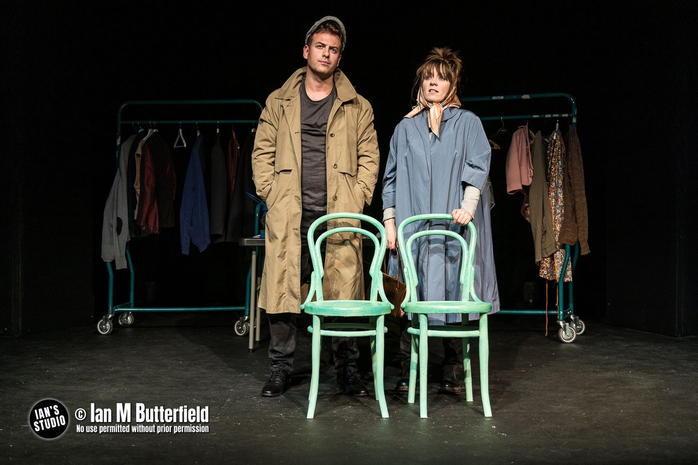 A couple on stage infront of 2 green clothes rails and behind 2 green bentwood chairs