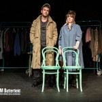 A couple on stage infront of 2 green clothes rails and behind 2 green bentwood chairs