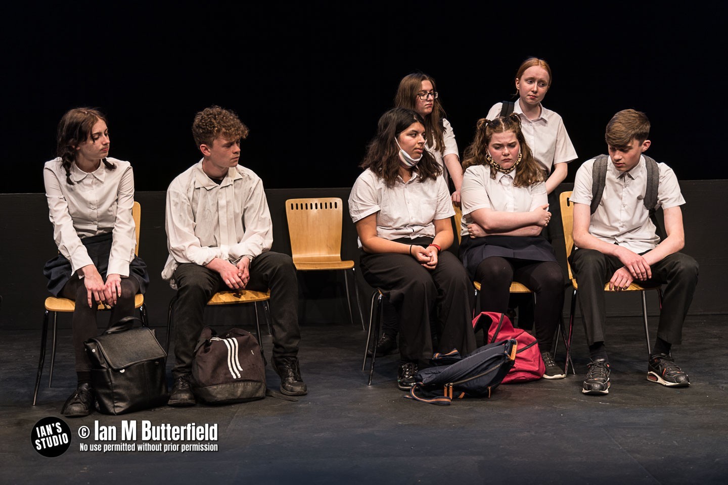 Lots of teenagers in school unforms sat on chairs