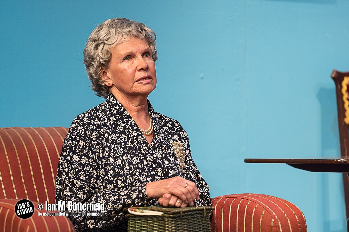 An old women sat on a red arm check with a sewing box in her lap