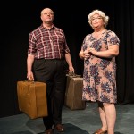 A man and women stood on a black stage with an old fashioned suitcase